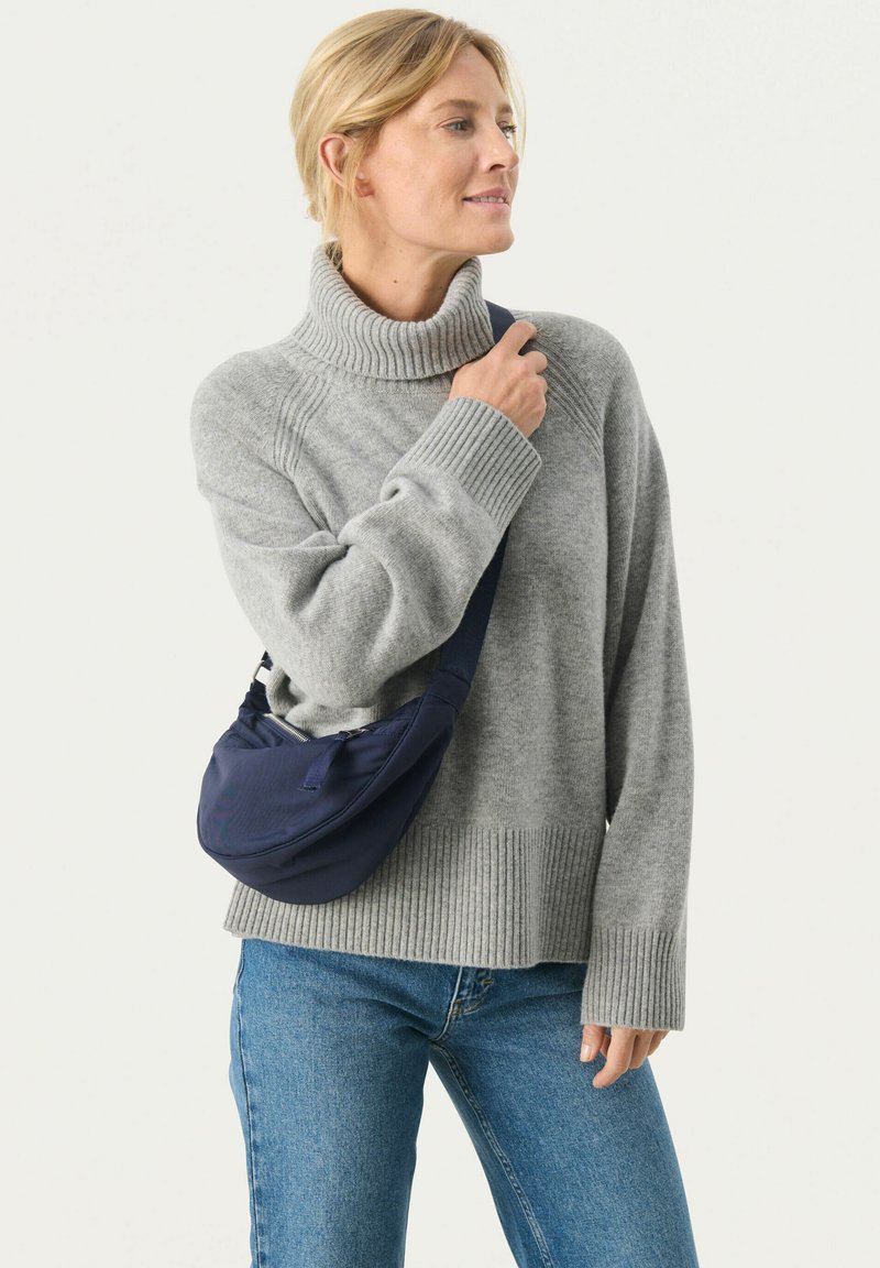 Maglione grigio a costine con collo alto abbinato a jeans di jeans azzurri. Una borsa a tracolla blu navy è indossata con una tracolla in tessuto.