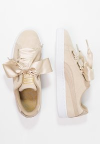 Sneakers in suede beige con lacci in satin oversize, suole in gomma bianca e una soletta testurizzata con un motivo geometrico. Dettaglio del logo dorato.