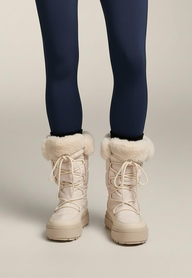 Roomkleurige sneeuwlaarzen met nepbontaccenten, veters en gestructureerde zolen. Gemaakt van waterbestendig materiaal met een gewatteerd ontwerp.