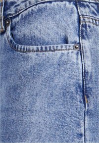 Vaqueros de denim azul claro con un acabado texturizado, que cuentan con un pequeño bolsillo delantero, botón de metal y costuras visibles a lo largo de las costuras.
