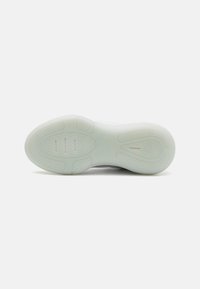 Semelle de chaussure de sport blanche avec une surface en caoutchouc texturée, présentant un motif en chevron et un logo de marque en relief. Matériau lisse et légèrement translucide.