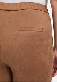 Brązowe zamszowe spodnie o miękkiej teksturze, z jedną tylną kieszenią i elastycznym pasem dla komfortu i łatwości noszenia.