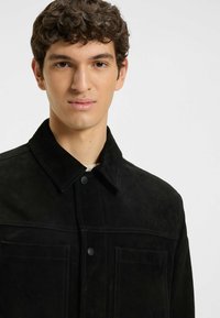 Svart mockajacka med spetsig krage, framfickor och kontrasterande sömmar. Slät textur med en skräddarsydd passform.