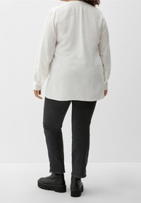 Witte blouse met lange mouwen en een geplooide halslijn, zachte textuur, gecombineerd met donkere denim jeans en stevige zwarte plateau boots.