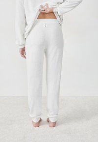 Lichtgrijze joggingbroek gemaakt van zachte stof. Beschikt over een elastische tailleband en geribbelde boorden. De achterkant heeft een label nabij de tailleband.