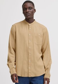 Langermet beige skjorte med høy krage, knappelukking foran og en lomme på venstre bryst, laget av lett stoff.