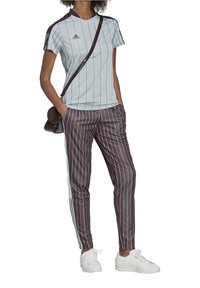 T-shirt de sport rayé bleu clair avec des accents violet foncé, associé à un pantalon rayé violet foncé. Baskets blanches et sac en bandoulière marron.