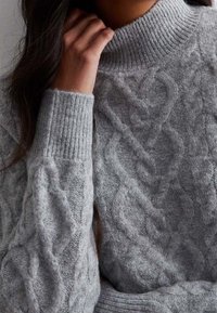 Grauer Kabelstrick-Turtleneck-Pullover mit gerippten Bündchen und Kragen. Verfügt über ein strukturiertes Muster und ein weiches, flauschiges Material.