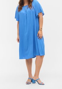 Blå klänning i knälängd med korta, svävande ärmar och en nyckelhålsurringning. Slätt tyg med en avslappnad passform. Matchad med blå klacksandaler.