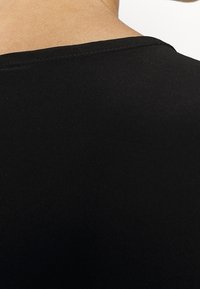 Haut en tissu noir avec une texture lisse et un col rond, montrant un gros plan de la zone du dos et des coutures des épaules.