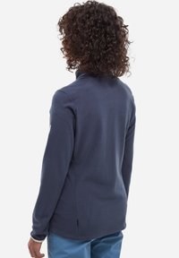 Pull en polaire bleu marine avec un col haut et une surface texturée, doté d'une fente latérale à l'ourlet et d'un détail de logo sur la manche.