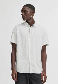 Camisa de manga corta en gris claro con bot�ón en la parte delantera, hecha de una tela texturizada. Presenta un collar y un detalle de contraste en el interior del escote.