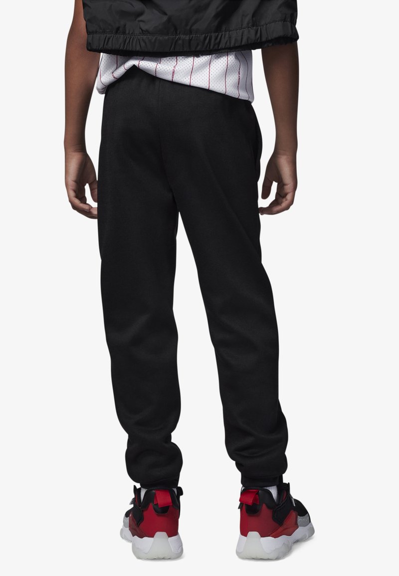 Pantalon de survêtement noir avec une coupe décontractée, doté d'une taille élastique. Accompagné de baskets rouges et noires avec des semelles blanches.