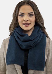 Sötétkék sál, puha anyagból készült, a nyak köré terítve. Sima textúrával és egyszerű dizájnnal rendelkezik, enyhén rojtos széllel.