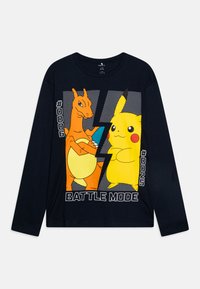 T-shirt à manches longues marine avec des graphiques colorés de Charizard et Pikachu, accompagné du texte "MODE COMBAT" et des numéros #006 et #025. Matière en coton.