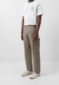 Krémové bavlněné tričko s potiskem na levé straně hrudníku, spárované se světle hnědými cargo kalhotami s bočními kapsami, obuté s krémovými teniskami.