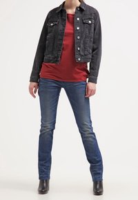 Svart denimjacka med knappar framtill, röd skjorta, blå smala jeans och svarta ankelboots. Släta material och figursydd design.