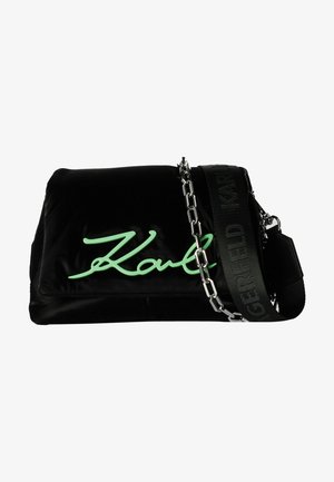 Bolso rectangular negro con logo verde en cursiva, cadena plateada y correa ancha de tela negra con un sutil patrón de texto.