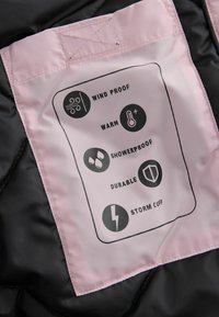 Tessuto nero con un'etichetta rosa che presenta cinque icone e il testo: antivento, caldo, impermeabile, durevole e polsino anti-tempesta.