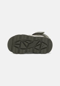 Semelle de chaussure de sport verte en caoutchouc à motif, avec des crampons profonds, des détails texturés et un design épuré. Inclut une sangle à velcro.