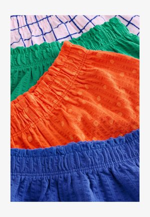 Farverige bomuldsshorts med elastiske taljebånd. Modellerne inkluderer grøn, orange med polkaprikker og blå teksturer, stablet sammen.