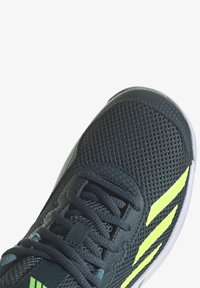 Baskets en maille gris foncé avec des accents jaunes, présentant une surface texturée, un design à lacets et une semelle blanche. Vue en gros plan.