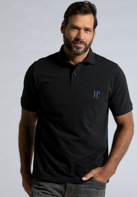 Kortærmet sort polo-shirt med krave, prydet med et diskret broderet logo i blå. Glat stof med en klassisk pasform, kombineret med mørke jeans.