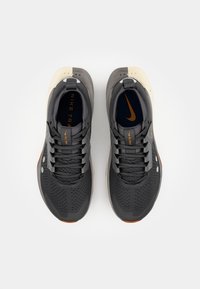 Baskets de sport grises avec un dessus texturé, des perforations pour la respirabilité et un accent orange sur la semelle. Comprend un col et une languette rembourrés.