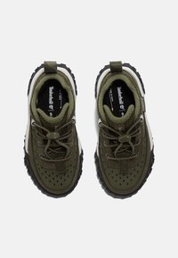 Baskets en textile vert avec des perforations, fermeture à lacets et une semelle en caoutchouc noir avec traction. Onglet de talon renforcé pour un enfilage facile.