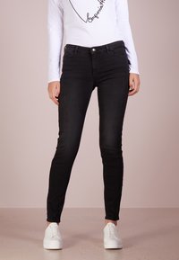 Svarta skinny jeans i jeansmaterial, med en klassisk femficksdesign och knappstängning, parat med en långärmad vit topp.
