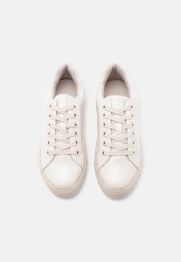 Valged lakknahast tennised, millel on sile pind, ümar ninaosa ja minimalistlik disain. Sisaldavad kuut silma ning kuldseid detaile.