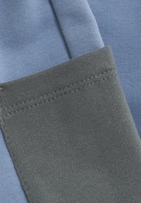 Bitar av bomullstyg i ljusblått och mörkgrått. Det blå tyget har en fin textur, medan det grå har en mjukare yta med synliga sömmar.