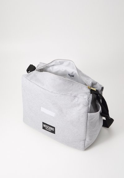 Borsetta in tessuto grigio con chiusura a zip, caratterizzata da un'etichetta logo nera e una tasca laterale. Texture liscia e forma rettangolare. L'interno presenta una fodera bianca.