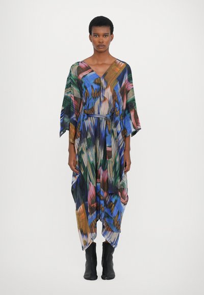 Multicolored kaftan with a V-neckline, featuring a vibrant abstract print, flowing silhouette, and wide sleeves. Worn with black ankle boots.