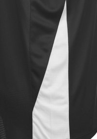 Maglia sportiva nera con pannello bianco diagonale, mesh testurizzato nelle sezioni nere e finitura liscia nel tessuto bianco.
