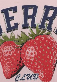 Un tissu rose présente un graphique de deux fraises rouges avec des feuilles vertes, accompagnées de lettres navy en gras épelant "BERRY" et du mot "CLUB" au bas.