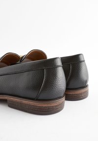 Mocassins en cuir noir avec une finition texturée, dotés d'un talon empilé marron et de détails de couture subtils à l'arrière.