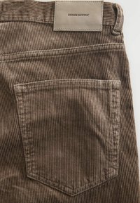 Hnedé kordové nohavice s vreckom na zadnej strane a pútkom na opasok, na páse s béžovou nášivkou s nápisom "DENIM SUPPLY".
