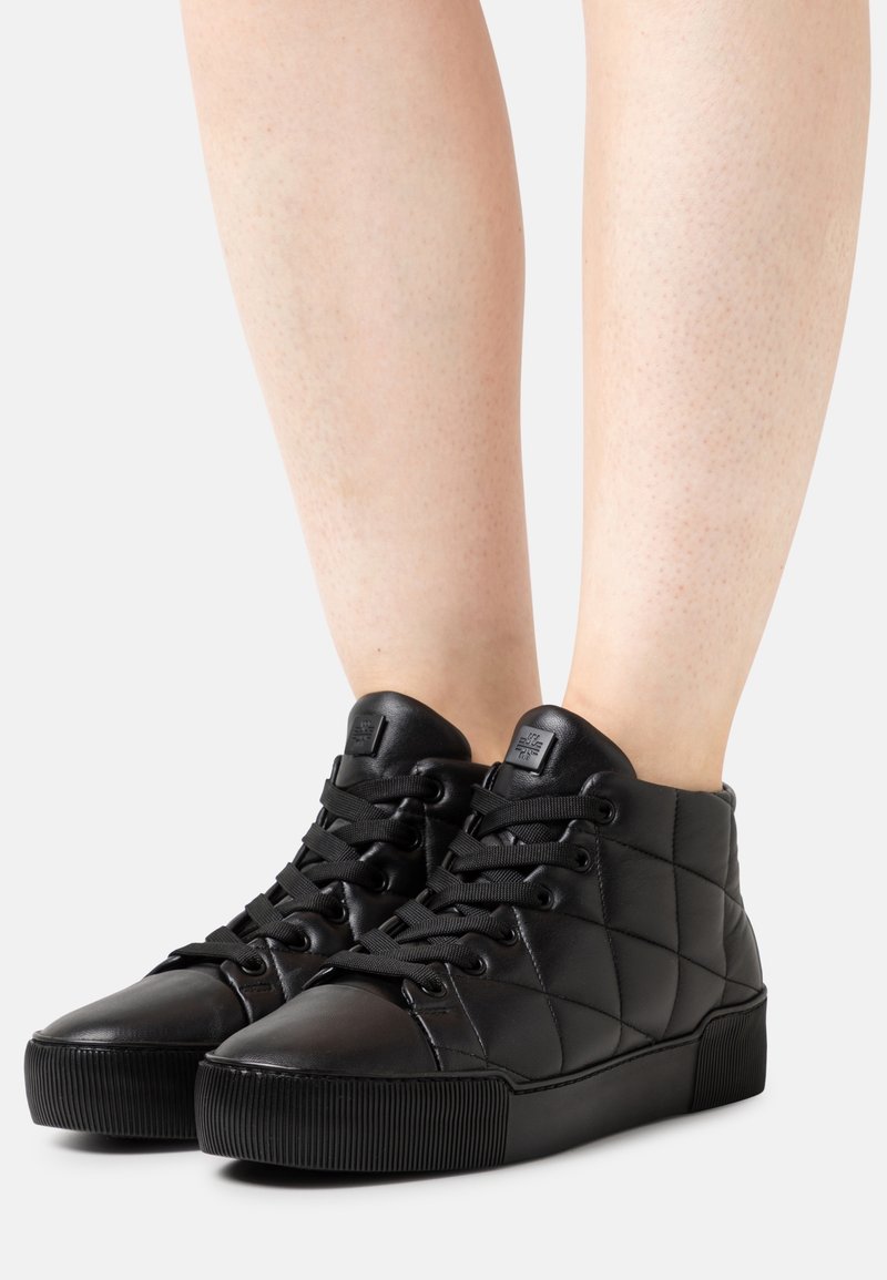 Black quilted high-top sneakers feature a smooth leather exterior, round toe, and textured rubber sole with prominent laces and branding detail.