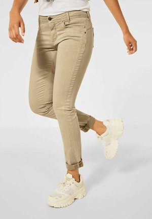 Chino en coton beige avec une coupe slim, poignets retroussés, poches avant et fermeture à bouton, associés à des baskets blanches chunky.