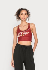 Czerwony sportowy crop top z kontrastowym logo i detalami. Posiada szerokie ramiączka oraz dopasowany krój, zestawiony z czarnymi spodniami dresowymi ze sznurkiem.