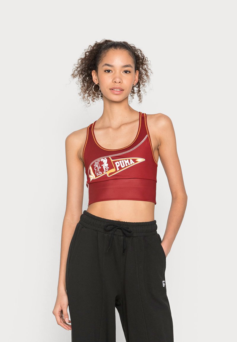Czerwony sportowy crop top z kontrastowym logo i detalami. Posiada szerokie ramiączka oraz dopasowany krój, zestawiony z czarnymi spodniami dresowymi ze sznurkiem.
