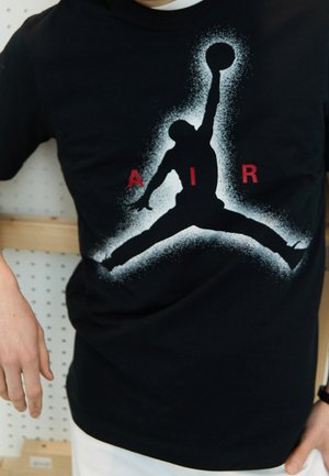 Sort bomulds T-shirt med en hvid og rød silhuet af en basketballspiller design og "AIR" tekst, glat tekstur og rund hals.