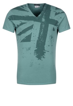 T-shirt à encolure en V et manches courtes en tissu de coton teal. Présente un motif estompé du drapeau Union Jack dans des tons teal plus foncés. Texture lisse.