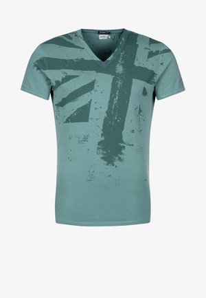 T-shirt à encolure en V et manches courtes en tissu de coton teal. Présente un motif estompé du drapeau Union Jack dans des tons teal plus foncés. Texture lisse.