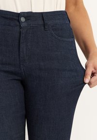 Mörkblå denimjeans med hög midja, standard femficksdesign och en lätt stretch för komfort, som visas när de dras i midjan.