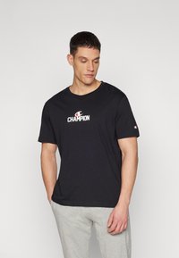 Sort Champion t-shirt lavet af bomuld, med rund hals og korte ærmer. Logo i rød og hvid på brystet og venstre ærme.