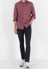 Camicia button-up bordeaux scuro con maniche arrotolate, abbinata a pantaloni neri slim-fit e sneakers bianche con accenti grigi.
