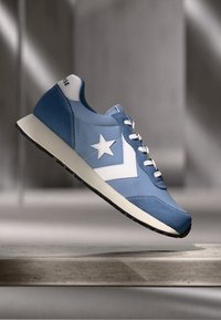 Light blue sneaker with white star emblem, smooth synthetic material, rounded toe, lace-up design, and black rubber sole.