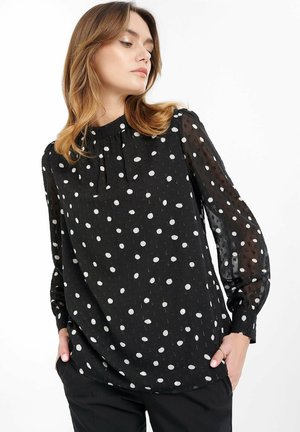 Blusa nera con pois bianchi, maniche lunghe trasparenti, scollatura rotonda con dettaglio a laccio, tessuto texturizzato, vestibilità rilassata.